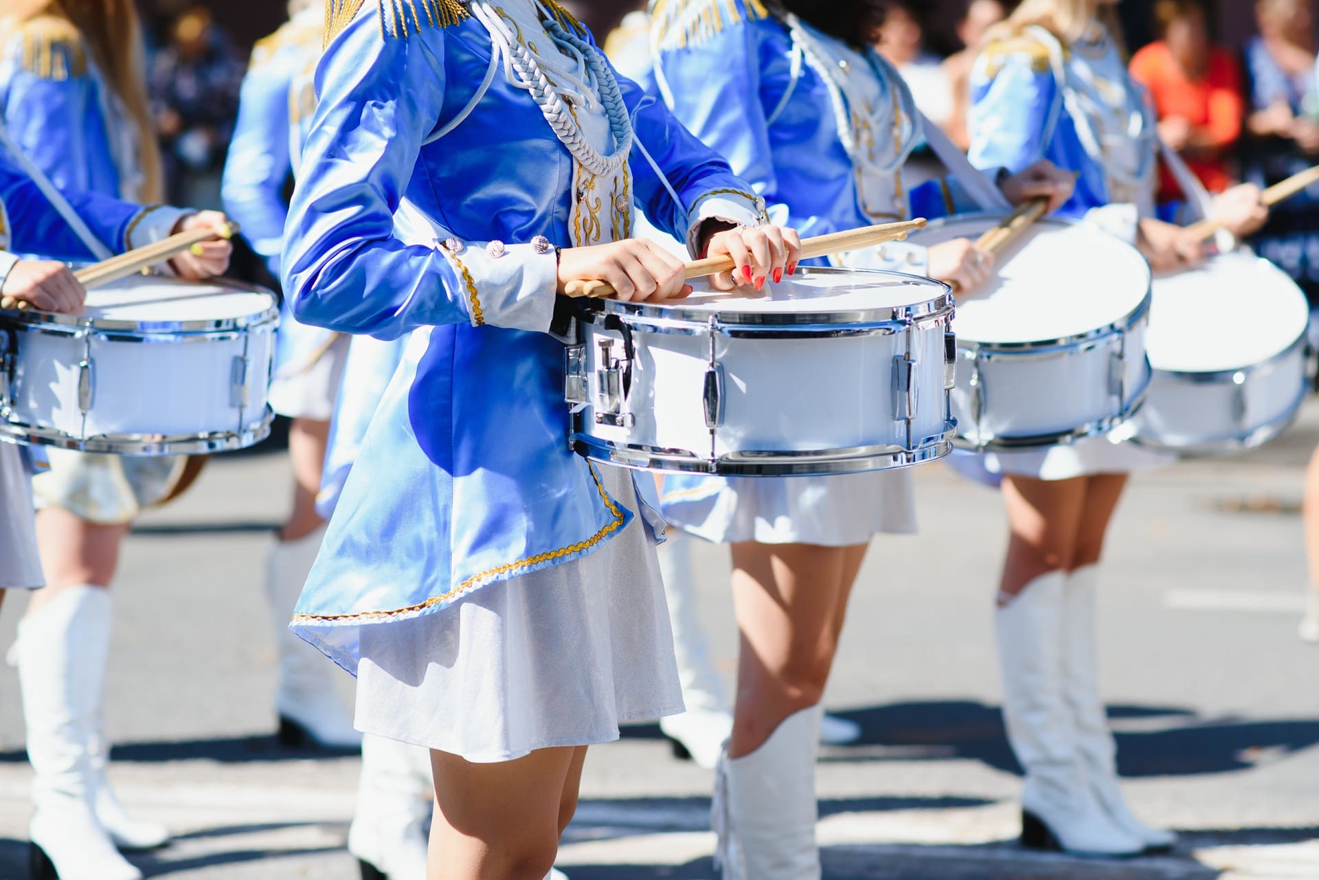 Group of marching band members in blue uniforms playing snare drums during a parade.